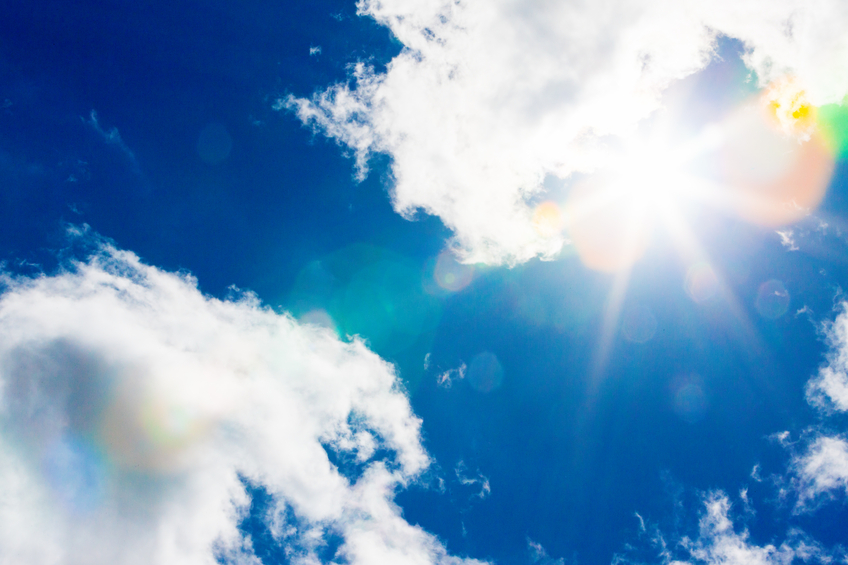 Looking up at the sun, high in the sky with dazzling radiating rainbow flare coming from it.