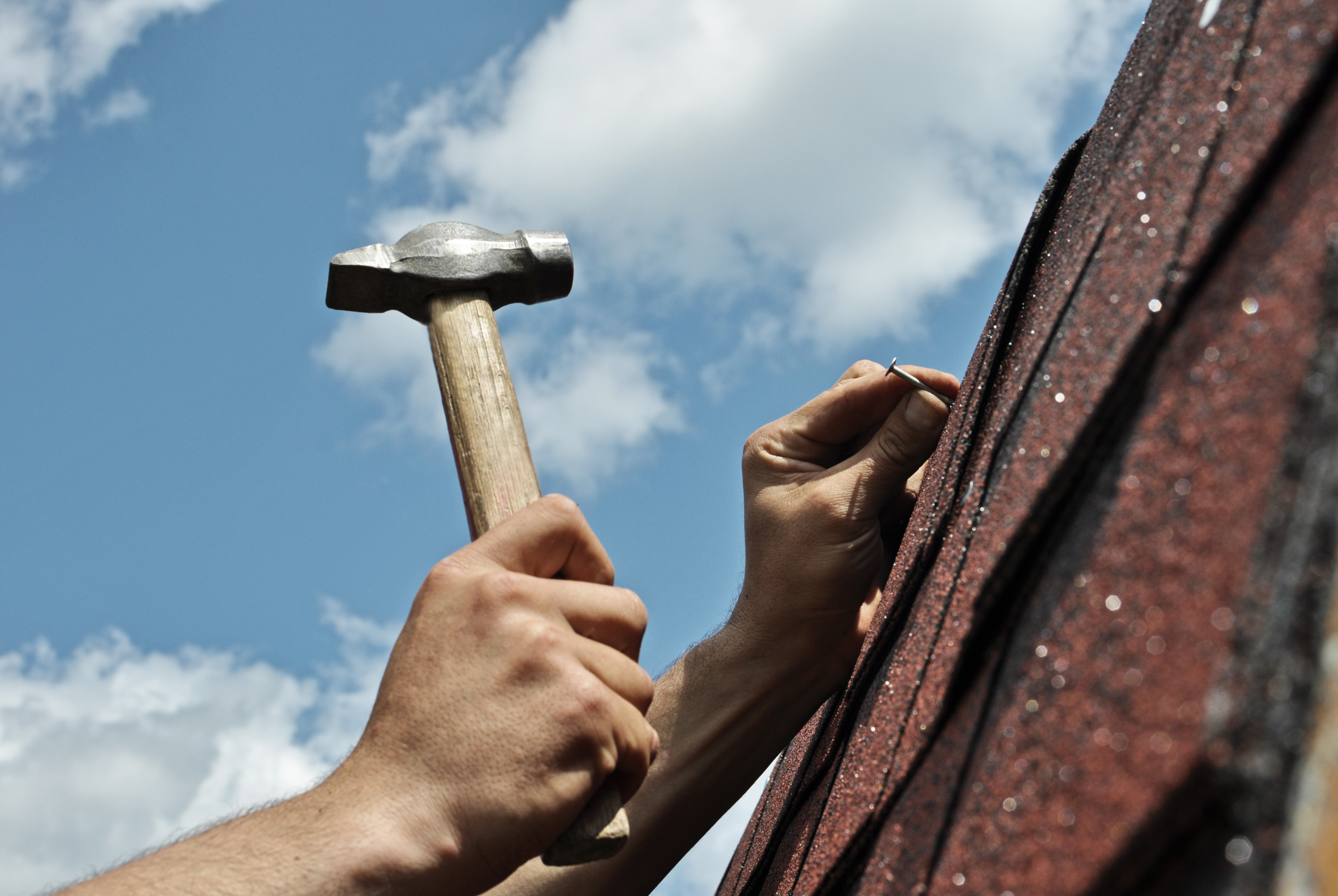 Roof repairs on background workers hands with hammer , focus on roof